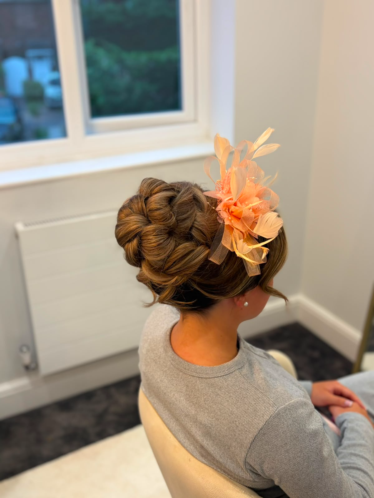 Braided occasion updo with a peach fascinator